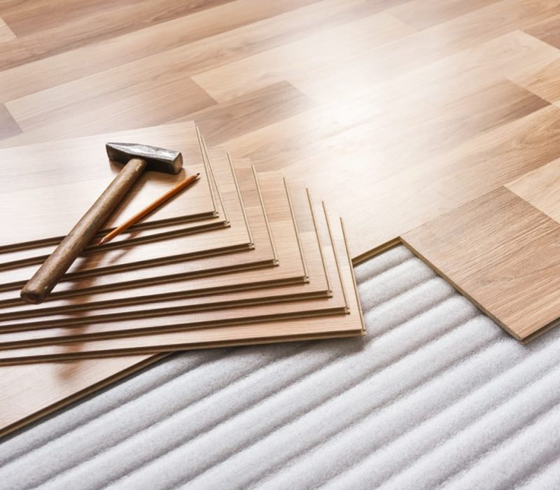 Installing laminated floor, detail on pile of wooden tiles, hammer and pencil, over white foam base layer